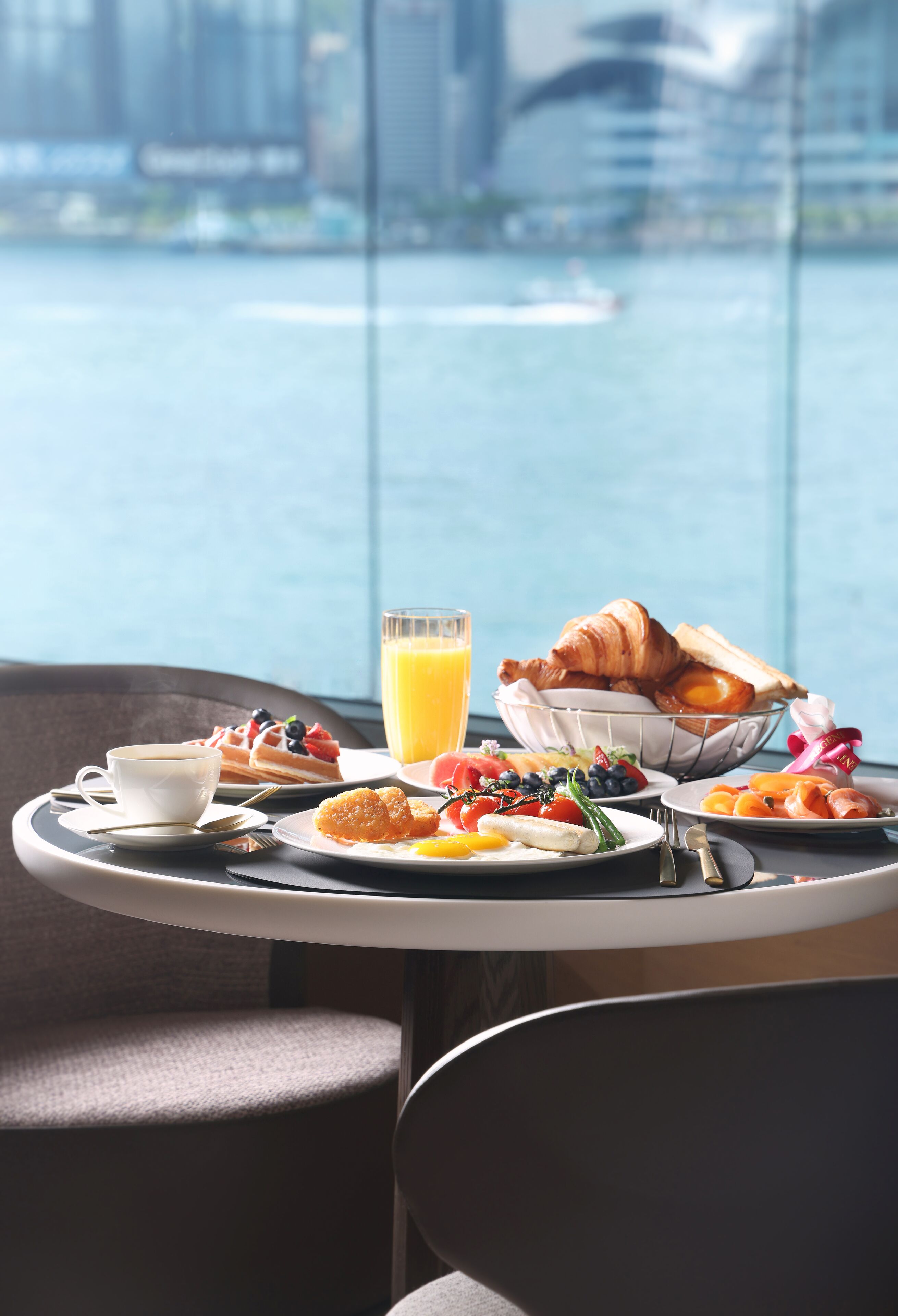 Un vassoio colazione con croissant, frutta e succo su un tavolo con vista sulla città.