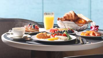 Un vassoio colazione con croissant, frutta e succo su un tavolo con vista sulla città.