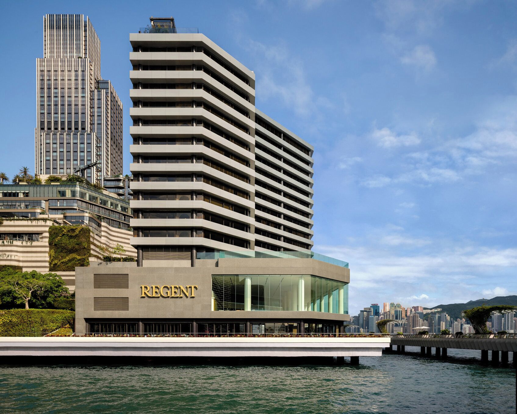 Hotel moderno com um destaque para o letreiro 'REGENT', localização à beira-mar e vista para o horizonte da cidade.