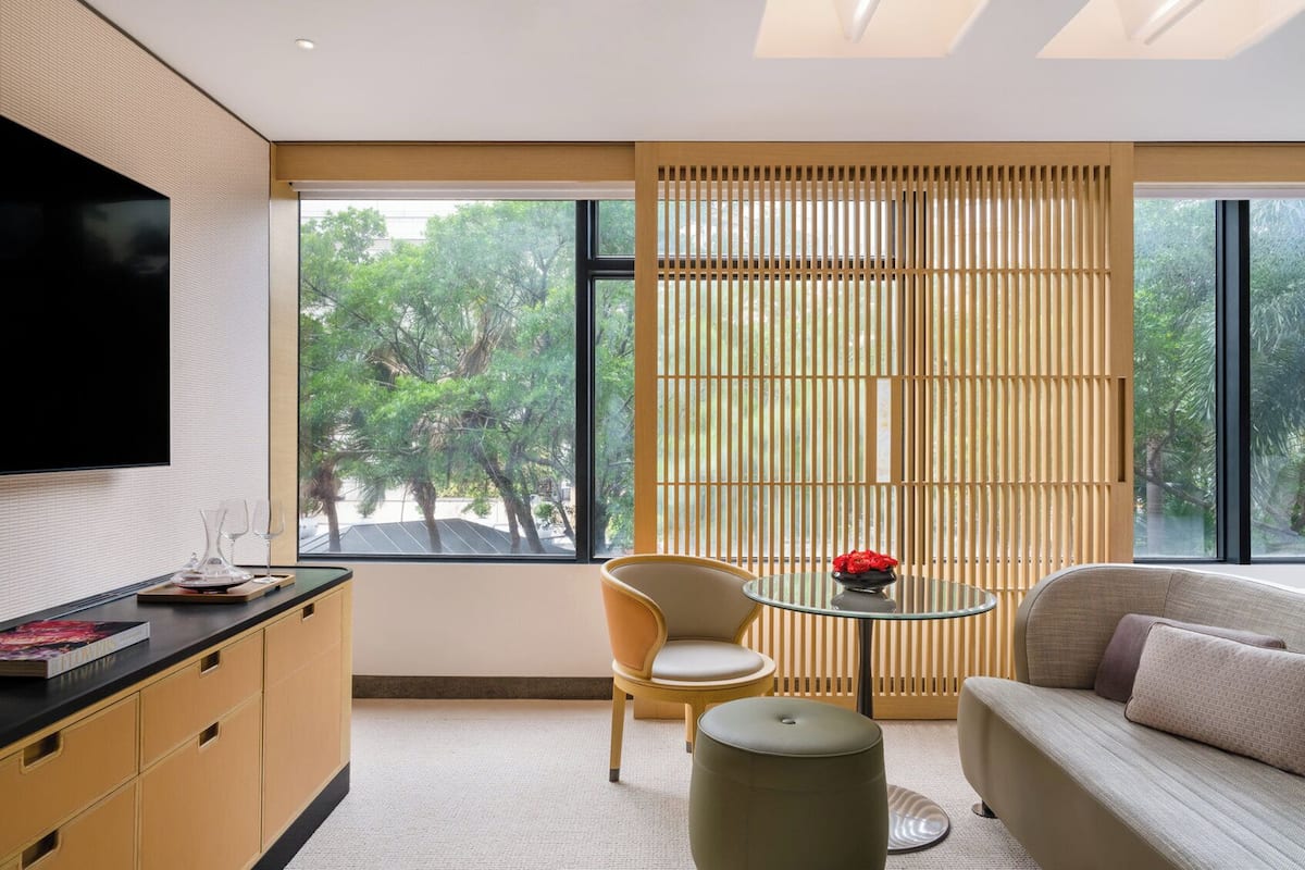 Un salon moderne avec un canapé, une table ronde en verre, un fauteuil et un téléviseur fixé au mur.