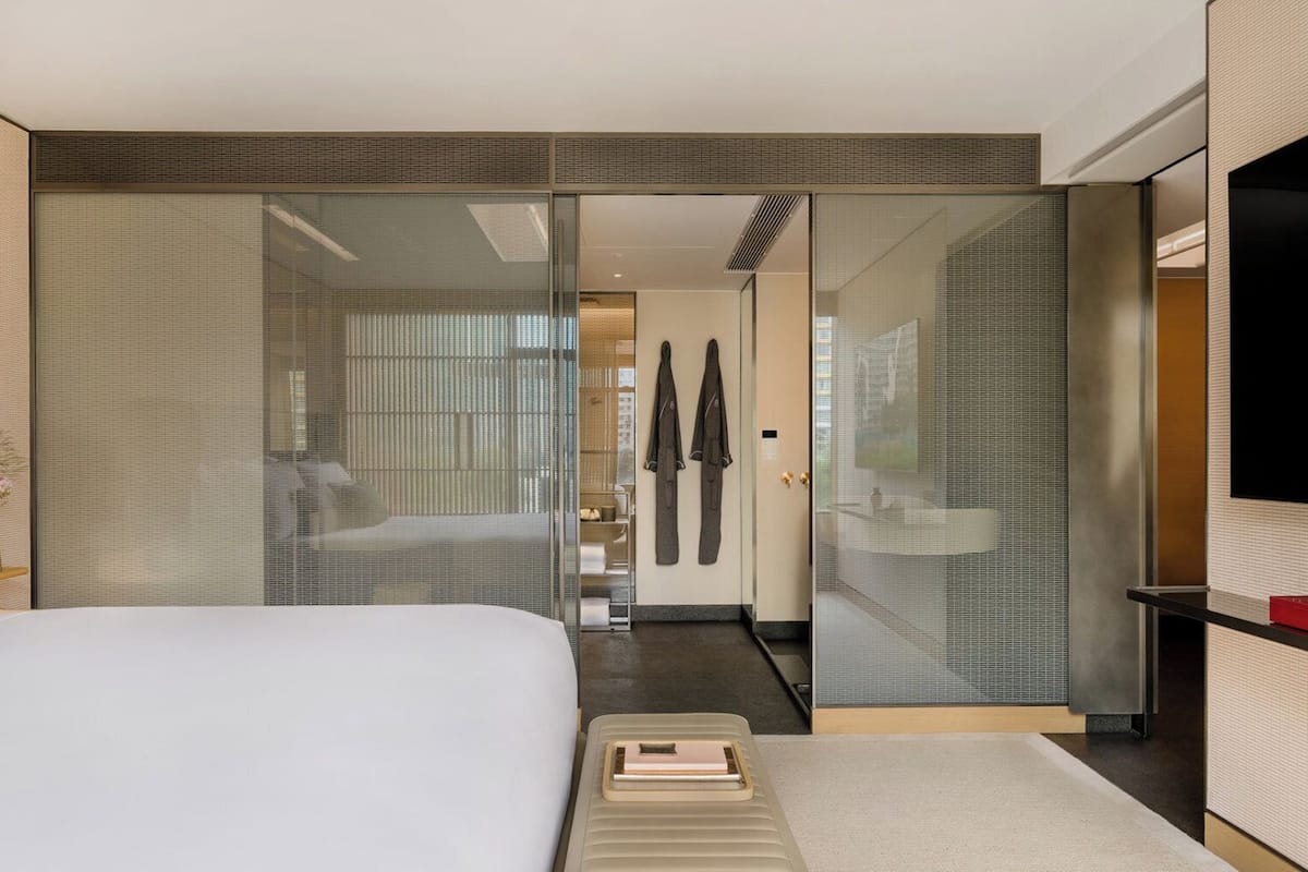 Une chambre d’hôtel moderne dotée d’un grand lit, d’une table de chevet, d’une télévision et d’une porte coulissante donnant accès à la salle de bain.