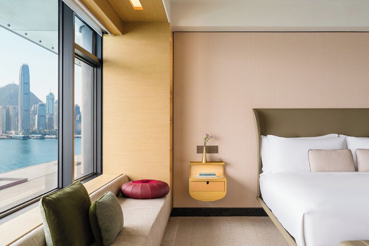 Une chambre d’hôtel avec une grande fenêtre, un lit, une table de chevet et une vue sur le paysage urbain.