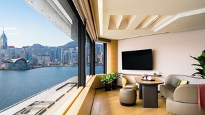 A modern hotel room with a city view, a flat-screen TV, a sofa, a small table, and a potted plant. - Regent Hong Kong (Kowloon)