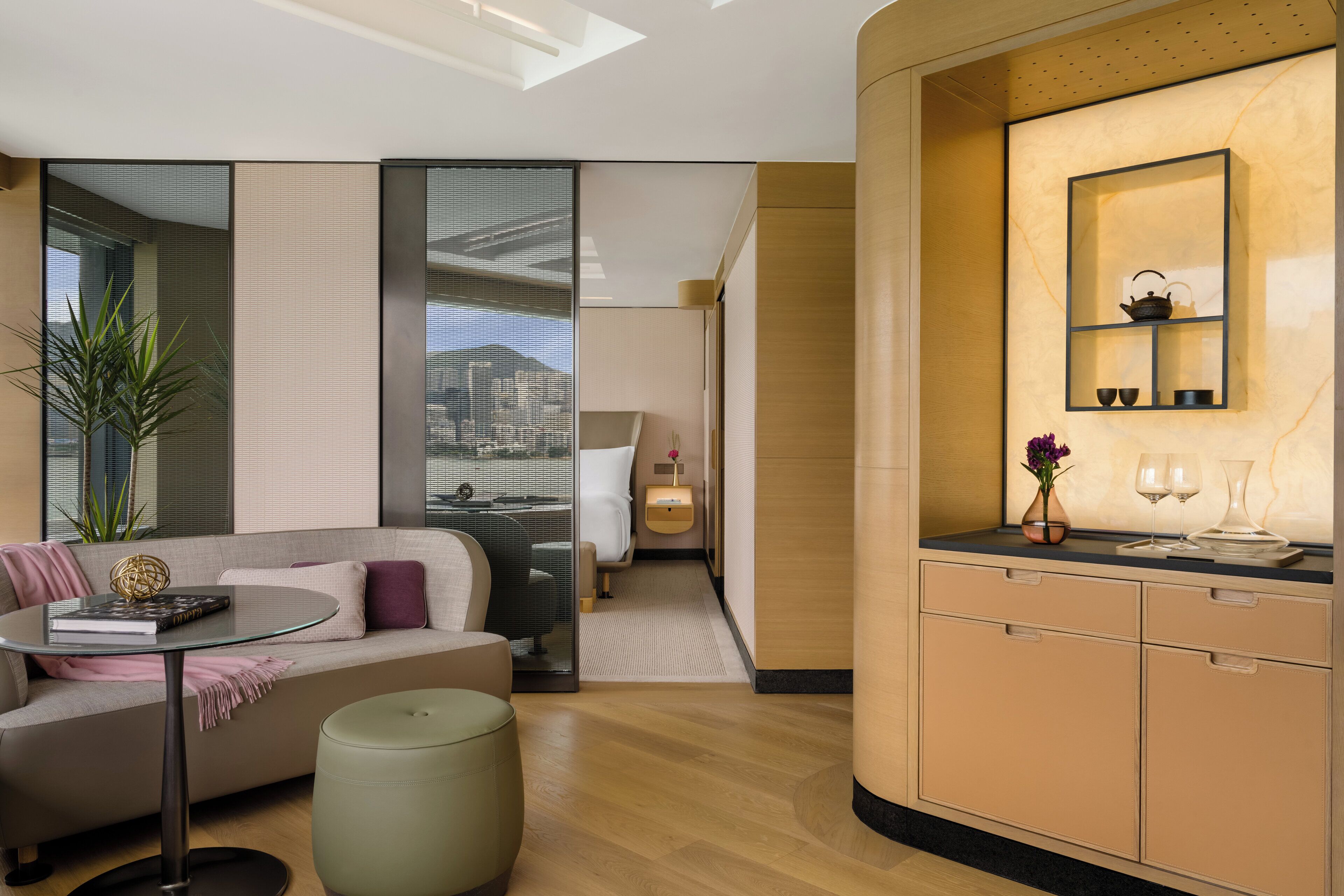 Camera d'albergo moderna con divano, un tavolino, un comodino e vista sulla città attraverso ampie finestre.