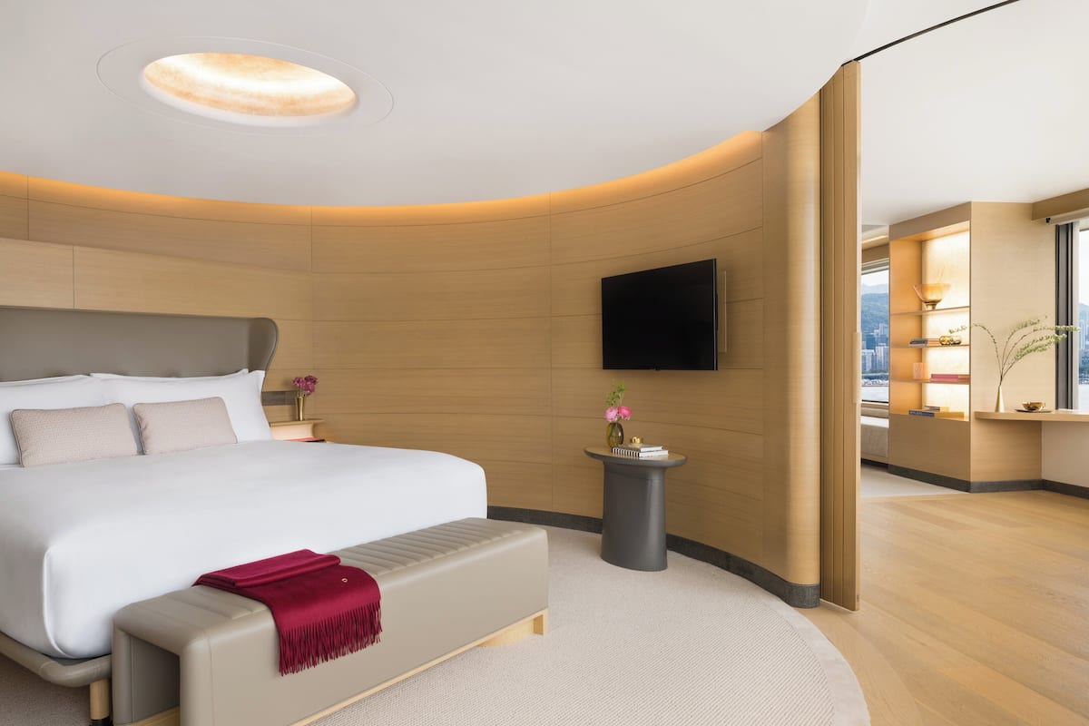 Une chambre d’hôtel moderne dotée d’un grand lit, d’une table de chevet, d’un téléviseur à écran plat et offrant une vue sur la ville par la fenêtre.