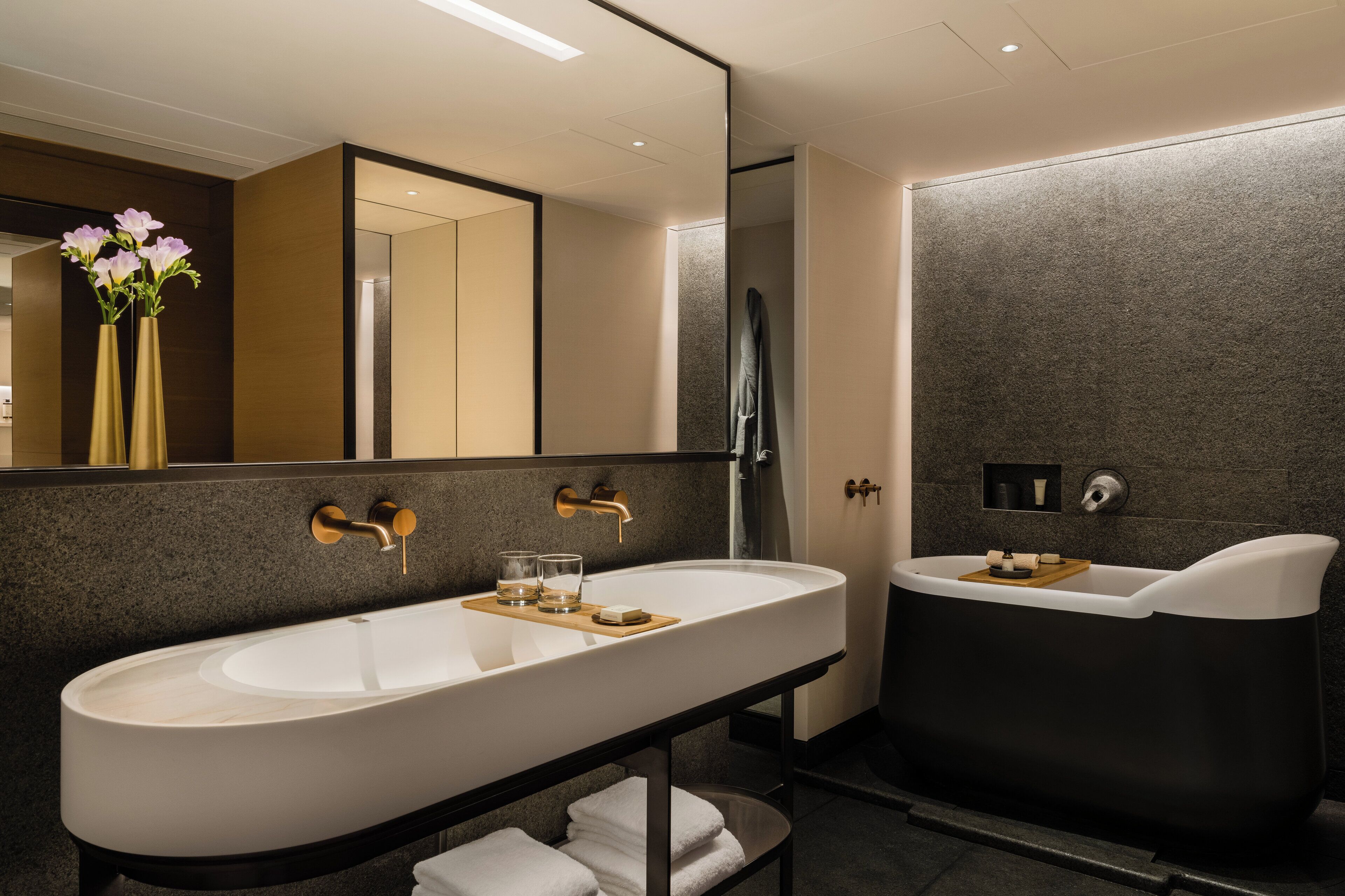 A modern bathroom with a large white sink, a black bathtub, and a mirror above the sink.