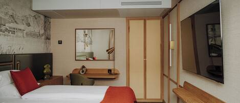 A hotel room with a bed, a desk, a mirror, a wardrobe, and a TV.