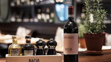 Une bouteille de Vino Rosso Bacio sur une table en bois, entourée d’autres bouteilles et d’une plante en pot.