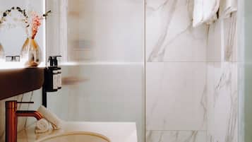 Un baño moderno con un lavamanos de mármol, cabina de ducha de vidrio y techo de madera.