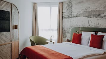 Una habitación de hotel con una cama, una silla verde, una mesita con un jarrón y un cuadro en la pared.