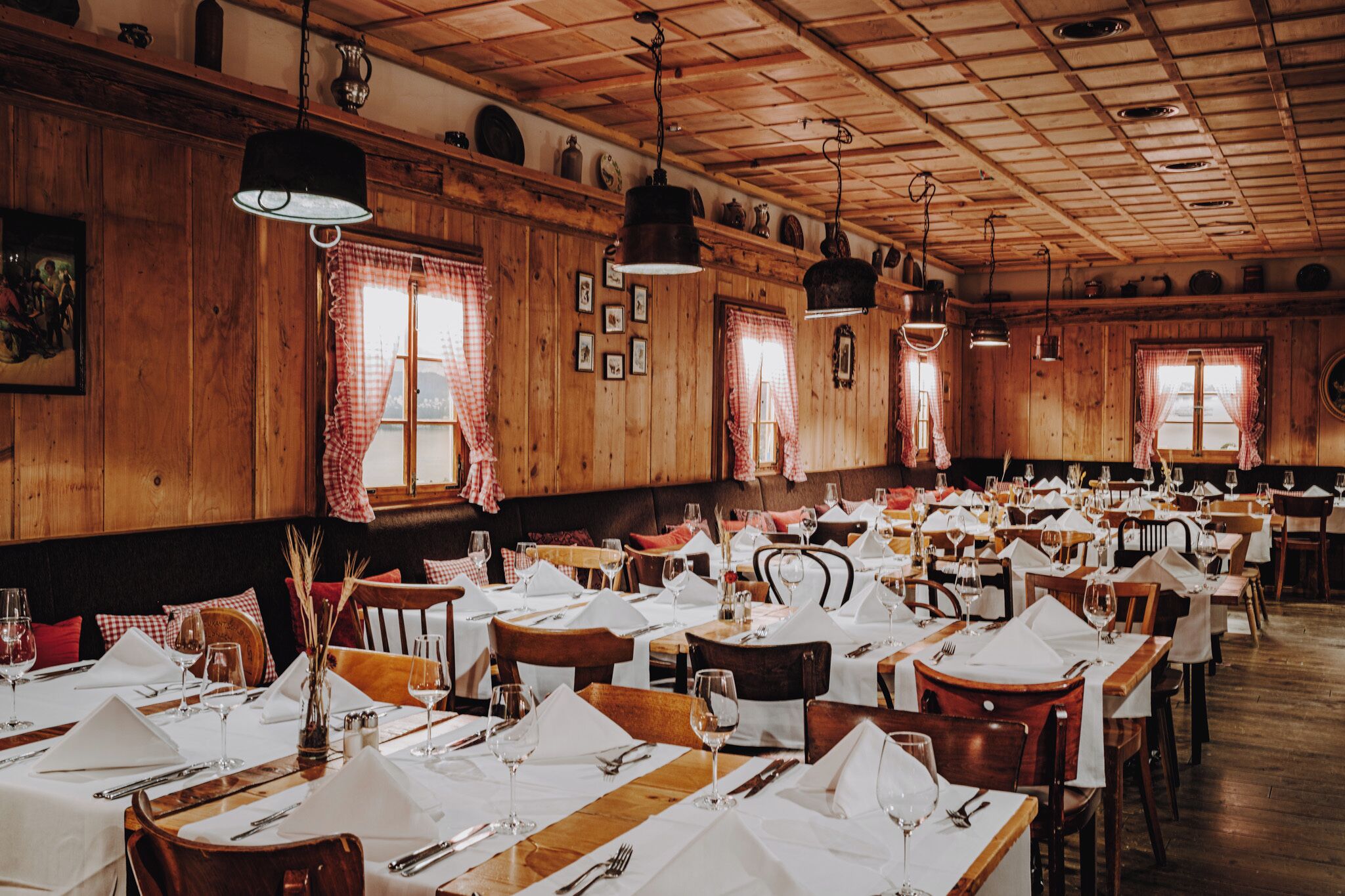 Un restaurante con paredes y techo de madera, mesas dispuestas con manteles blancos y lámparas colgantes.