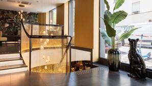 A modern lobby with a glass staircase, a large plant, and a decorative vase. - Prince Albert Lyon Bercy (Paris)