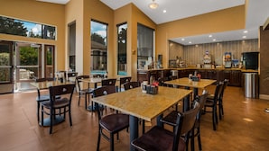 Un vaste espace intérieur aménagé en salle à manger, avec de nombreuses tables et chaises, de grandes fenêtres et un coin cuisine.