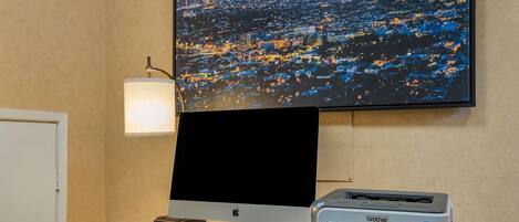 A desk with a desktop computer, a printer, a keyboard, a mouse, and a monitor displaying a cityscape.