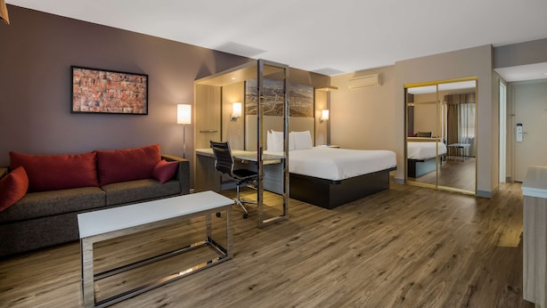 Une chambre d’hôtel moderne équipée d’un canapé, d’un bureau, d’un lit et d’un grand miroir.