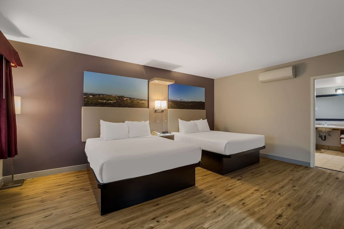 Habitación de hotel con dos camas, una mesita de noche, una lámpara y un ventanal con vistas a la ciudad.