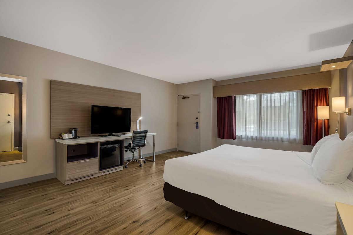 Una habitación de hotel con una cama grande, un escritorio con televisor y una ventana con cortinas.