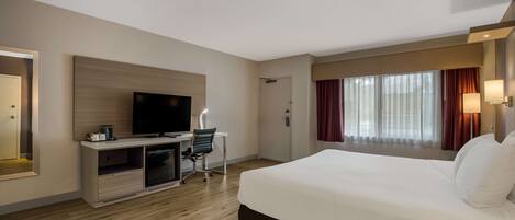 A hotel room with a large bed, a desk with a TV, and a window with curtains.