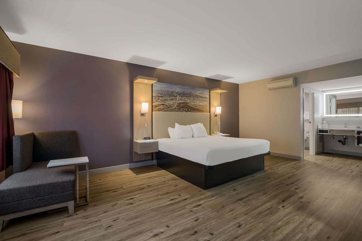 Una habitación de hotel moderna con una cama grande, un sofá pequeño, una mesita de noche y un televisor fijado a la pared.