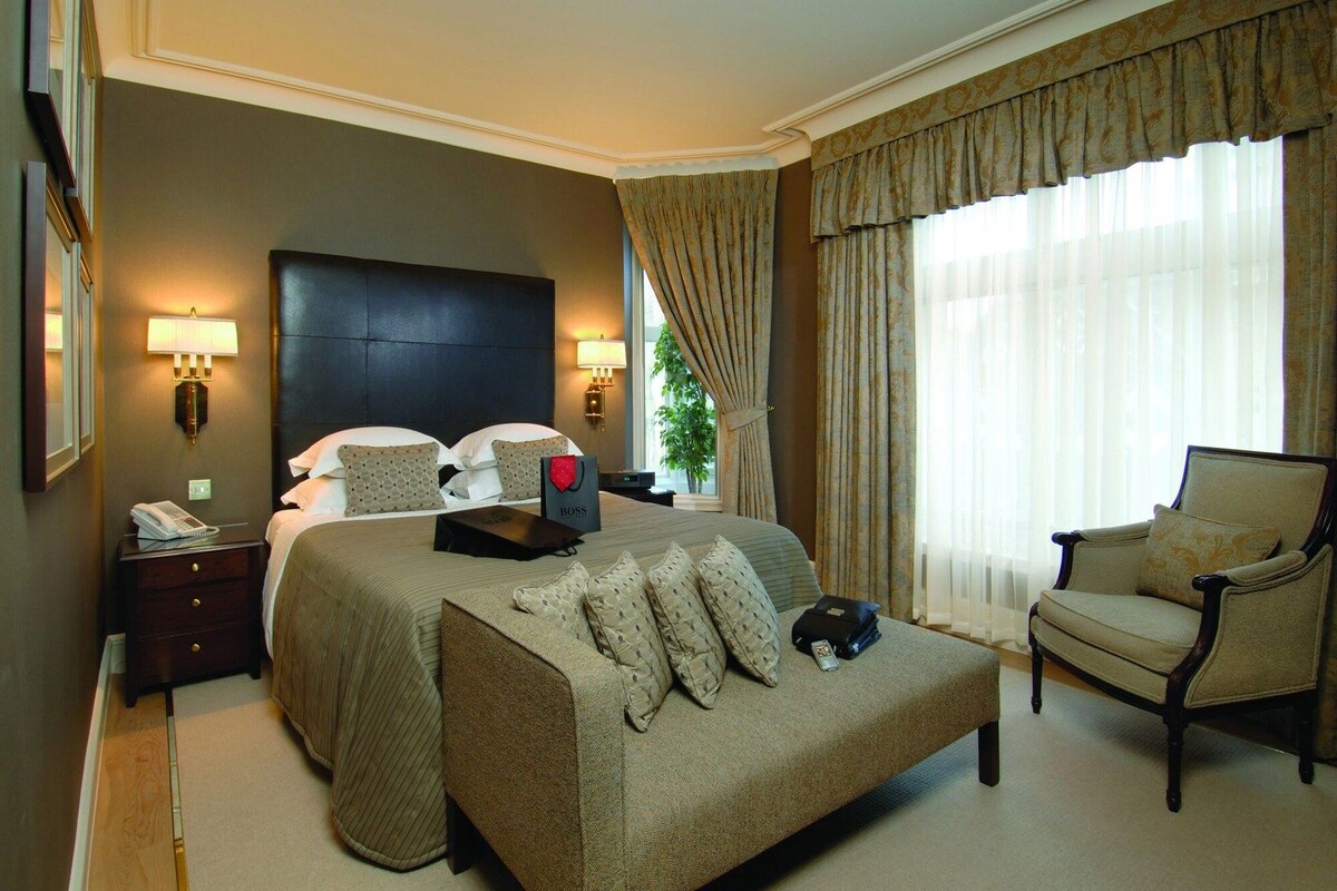 Een hotelkamer met een groot bed, een stoel, een nachtkastje met telefoon en een lamp.