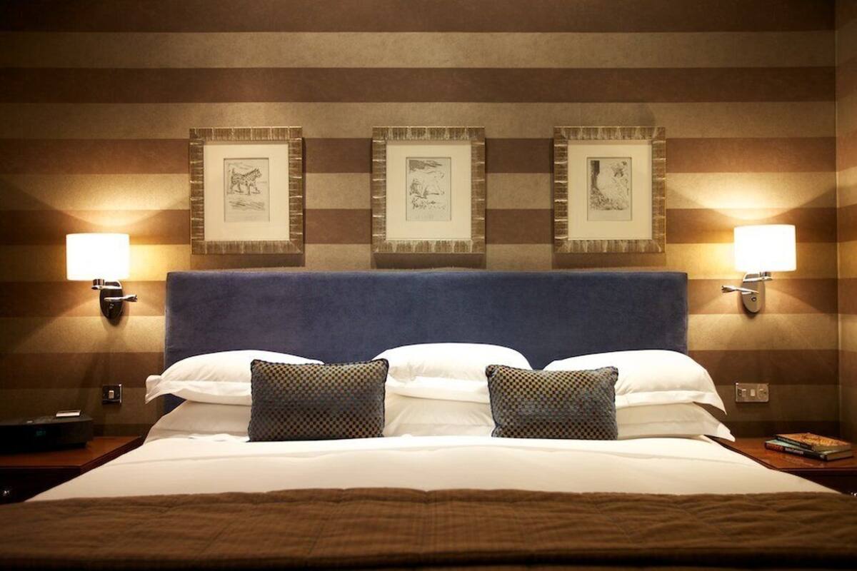 A hotel room with a large bed, two wall-mounted lamps, and three framed pictures on the wall.