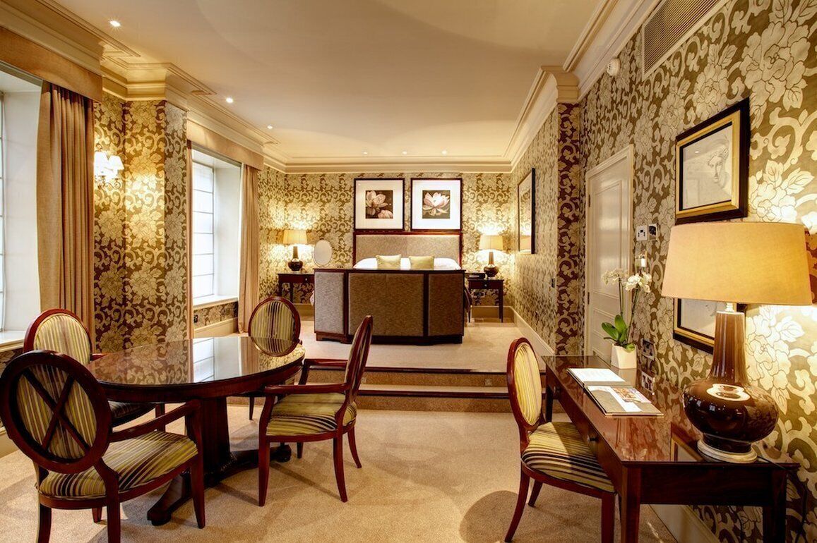 A hotel room with a dining area, a sofa bed, and a large window.