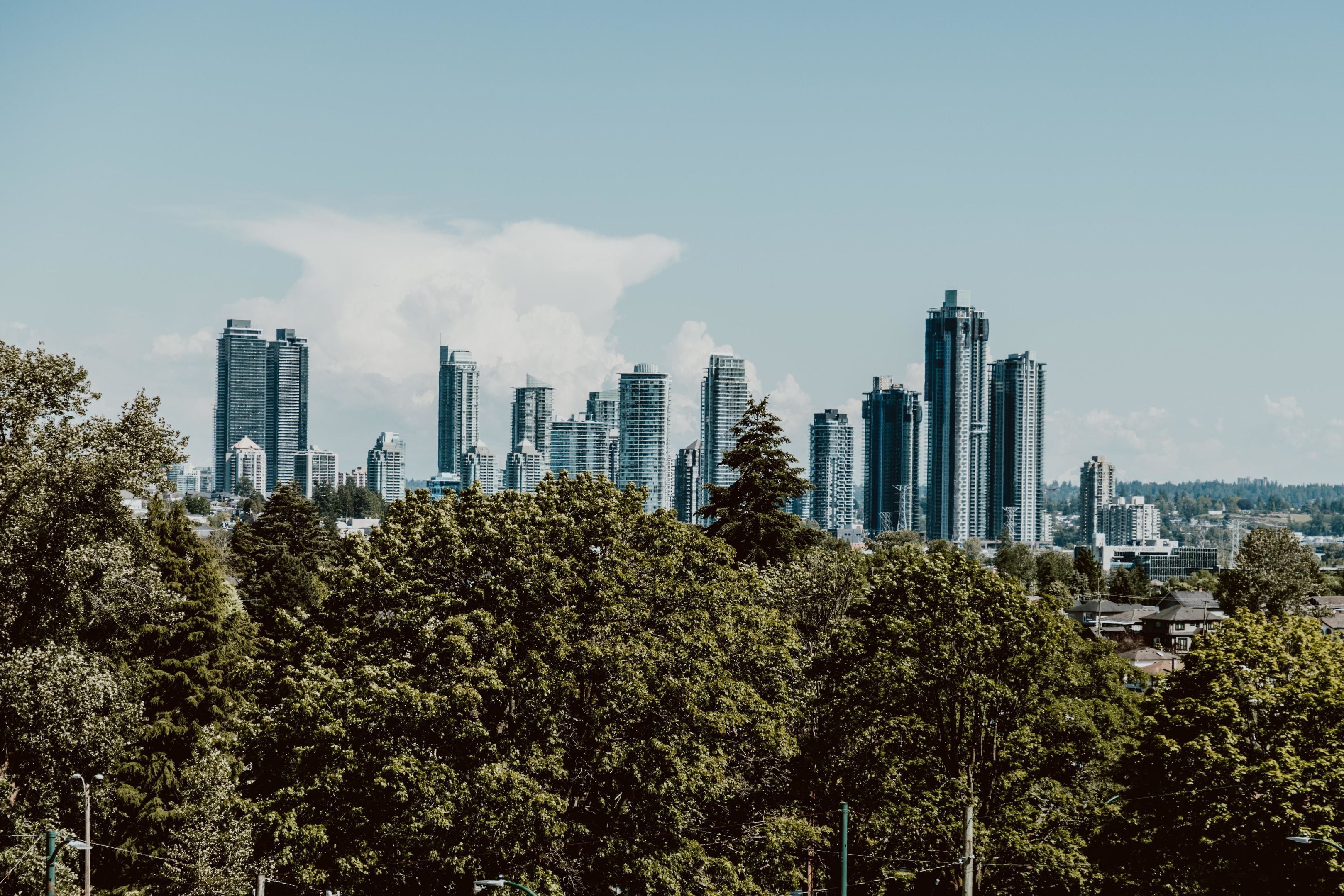 A city skyline with multiple high-rise buildings, trees in the foreground, and a clear sky.