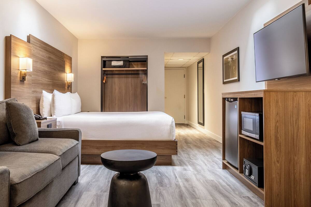 A hotel room with a bed, a sofa, a TV, a minibar, and a wooden headboard.
