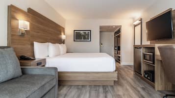 A hotel room with a bed, a sofa, a TV, a microwave, and a wooden headboard.