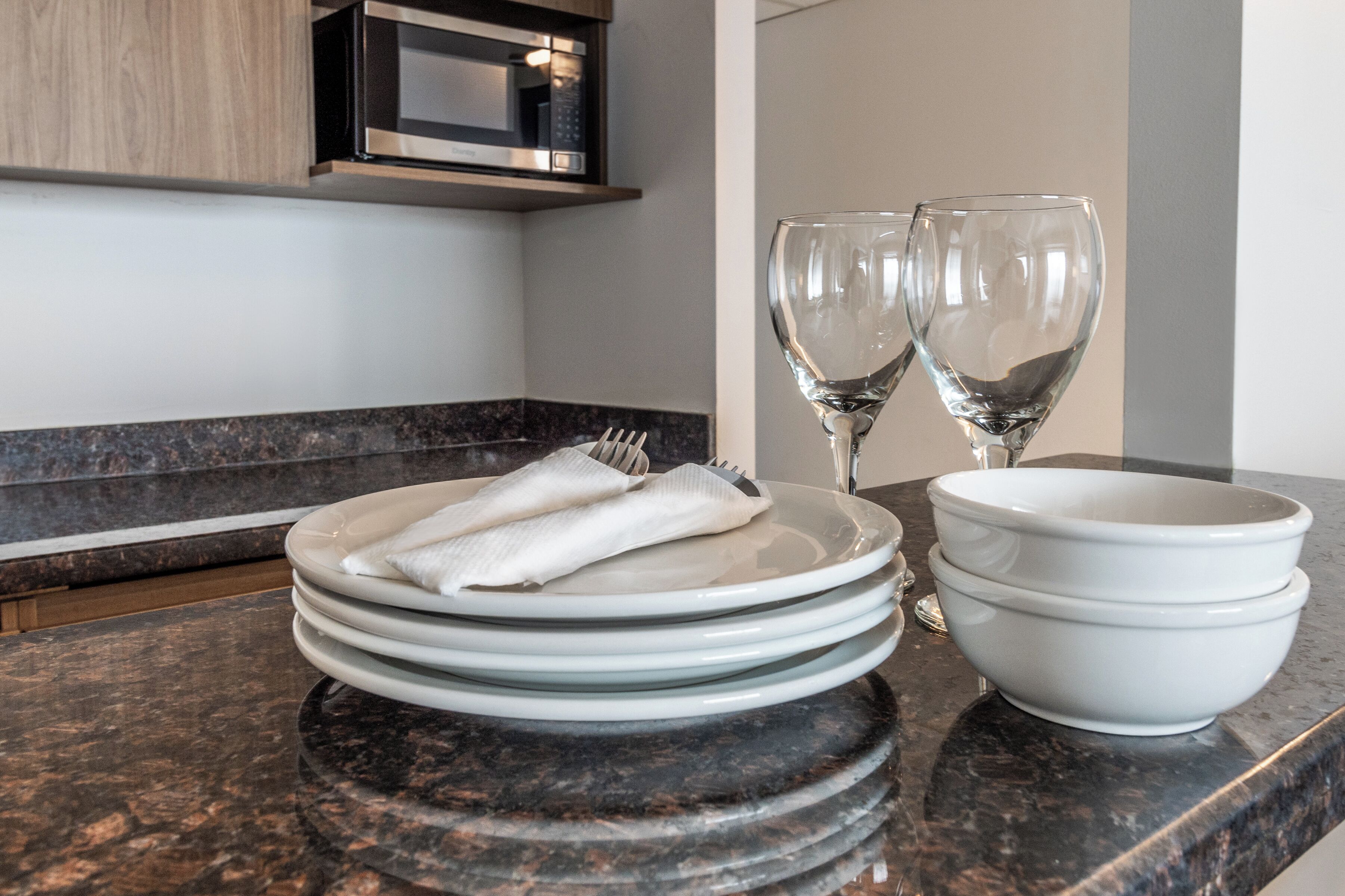 A kitchen counter with stacked plates, a bowl, and two wine glasses.