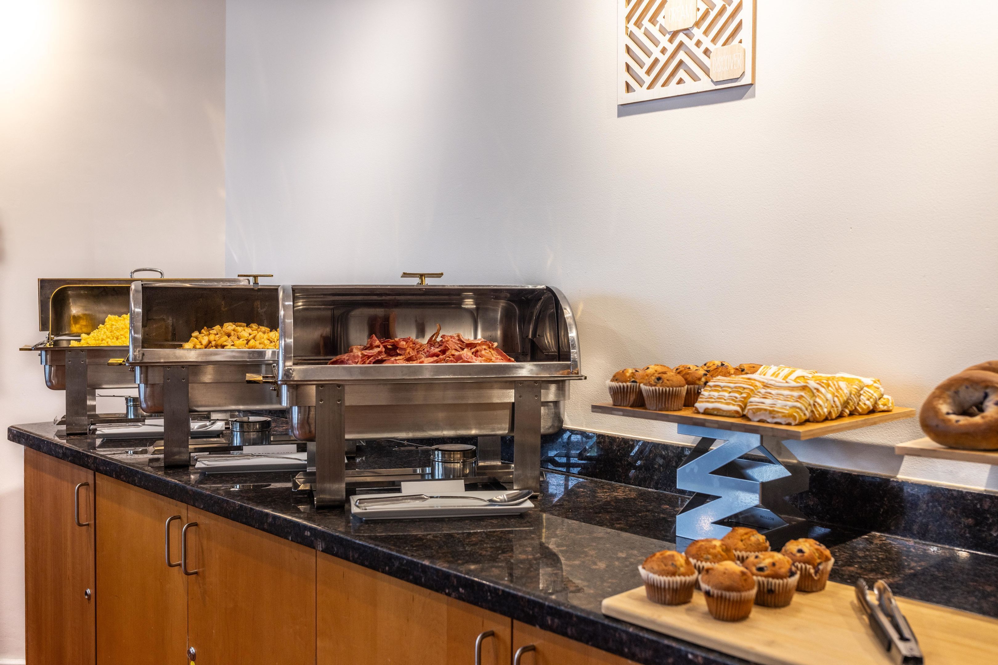 A buffet setup with various food items and a cutting board with muffins.