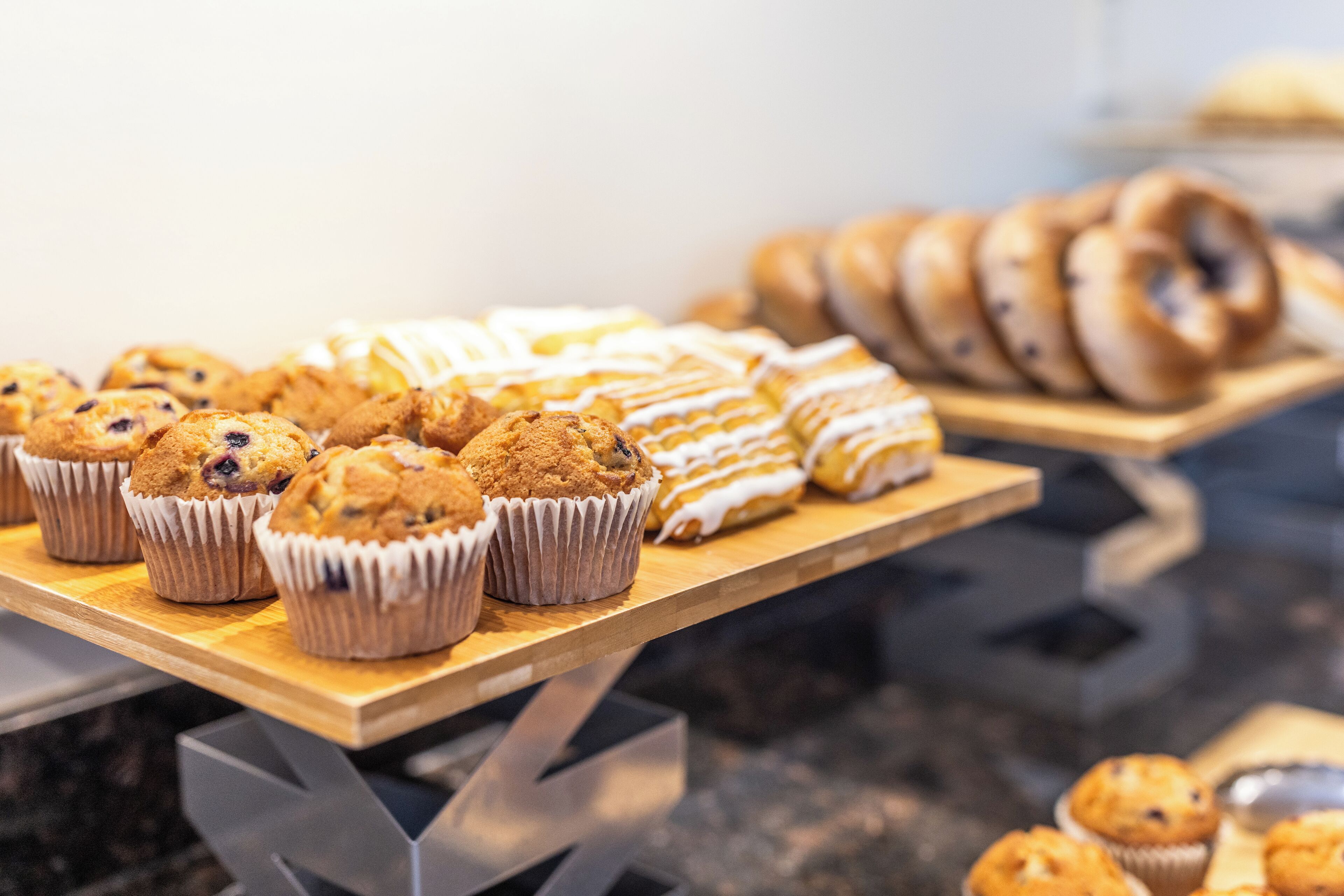 A variety of baked goods displayed on a wooden table, including muffins and bagels.
