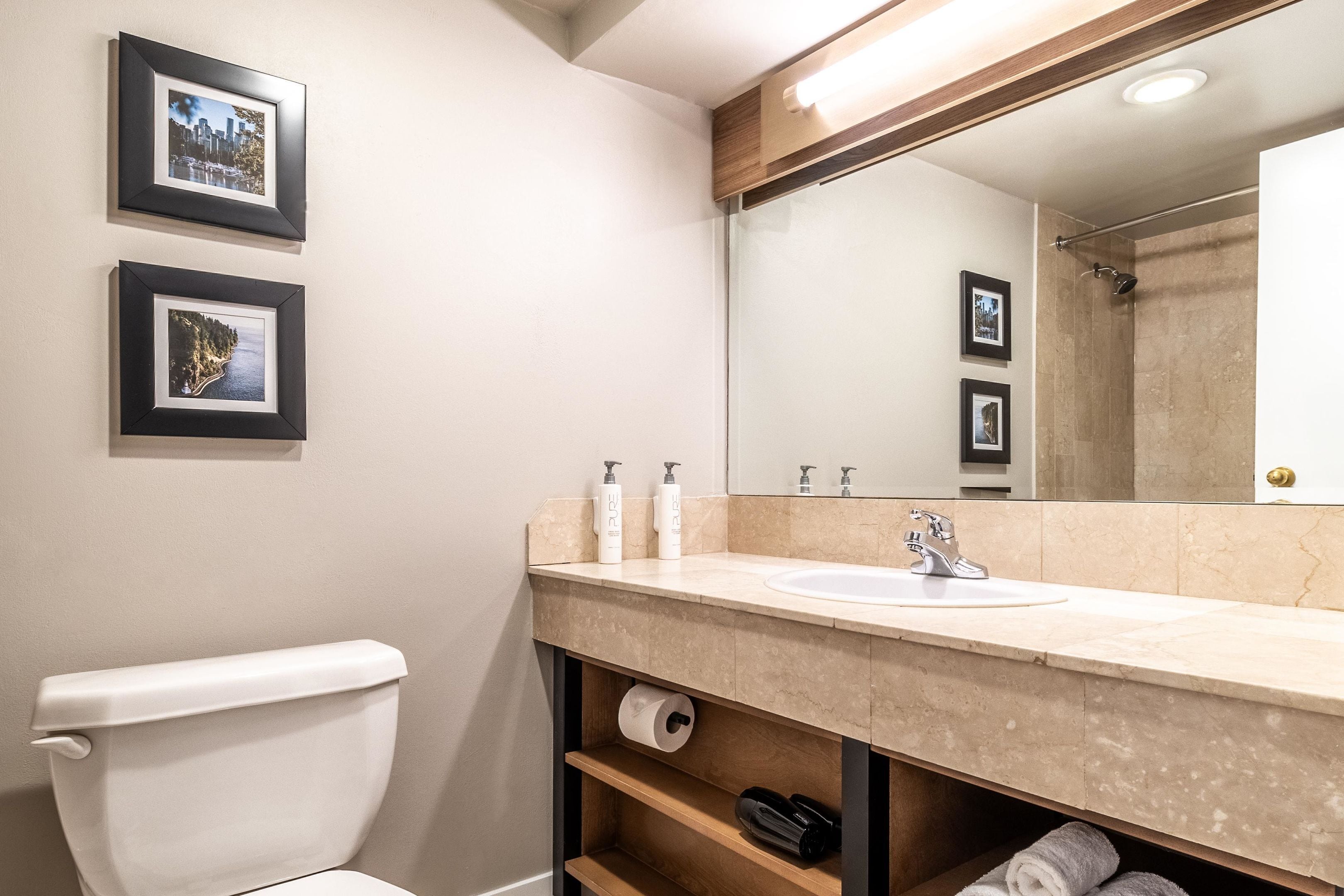 A modern bathroom with a toilet, sink, and mirror. There are framed pictures on the wall.