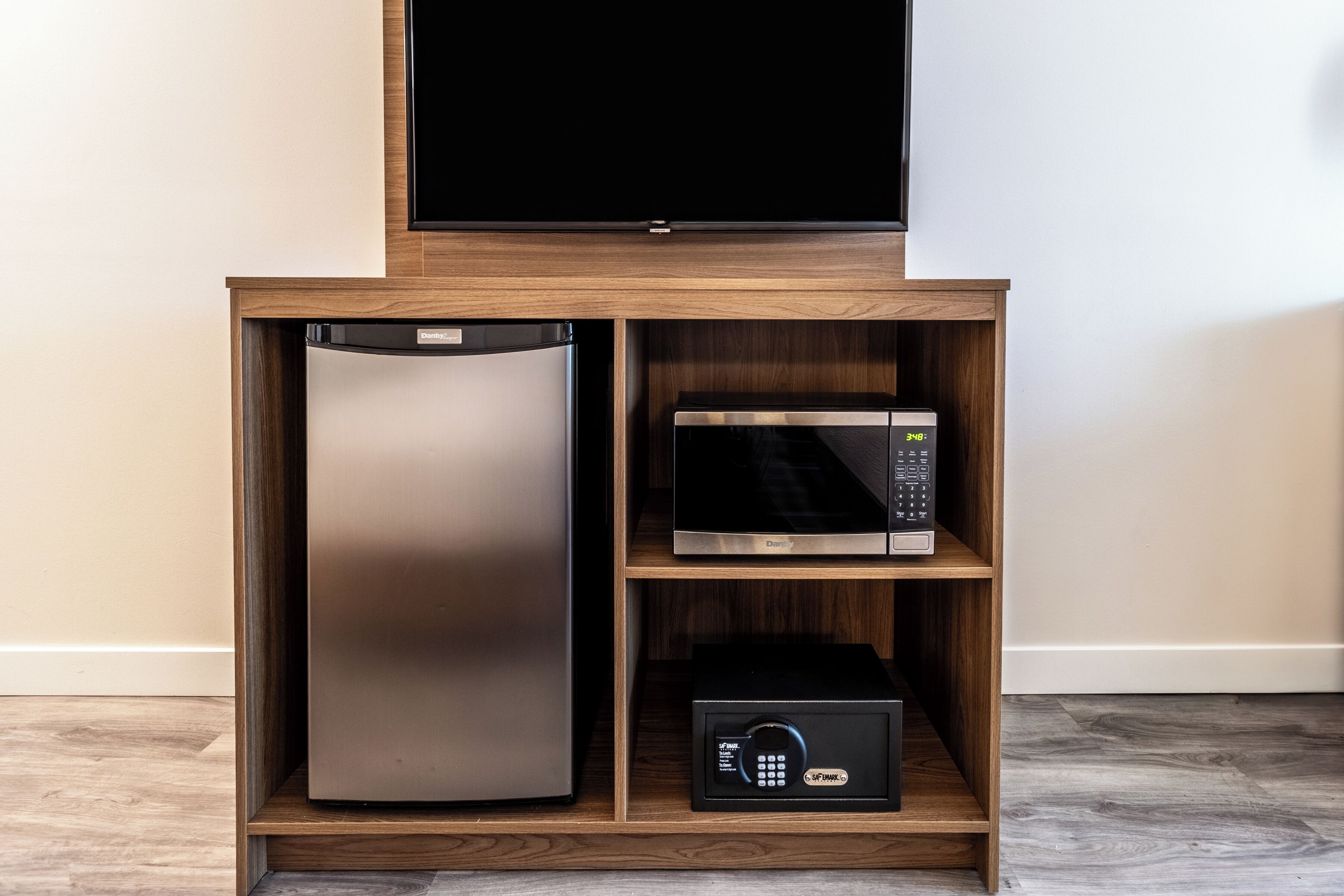 A wooden cabinet with a stainless steel refrigerator, a microwave, and a black box with a keypad.
