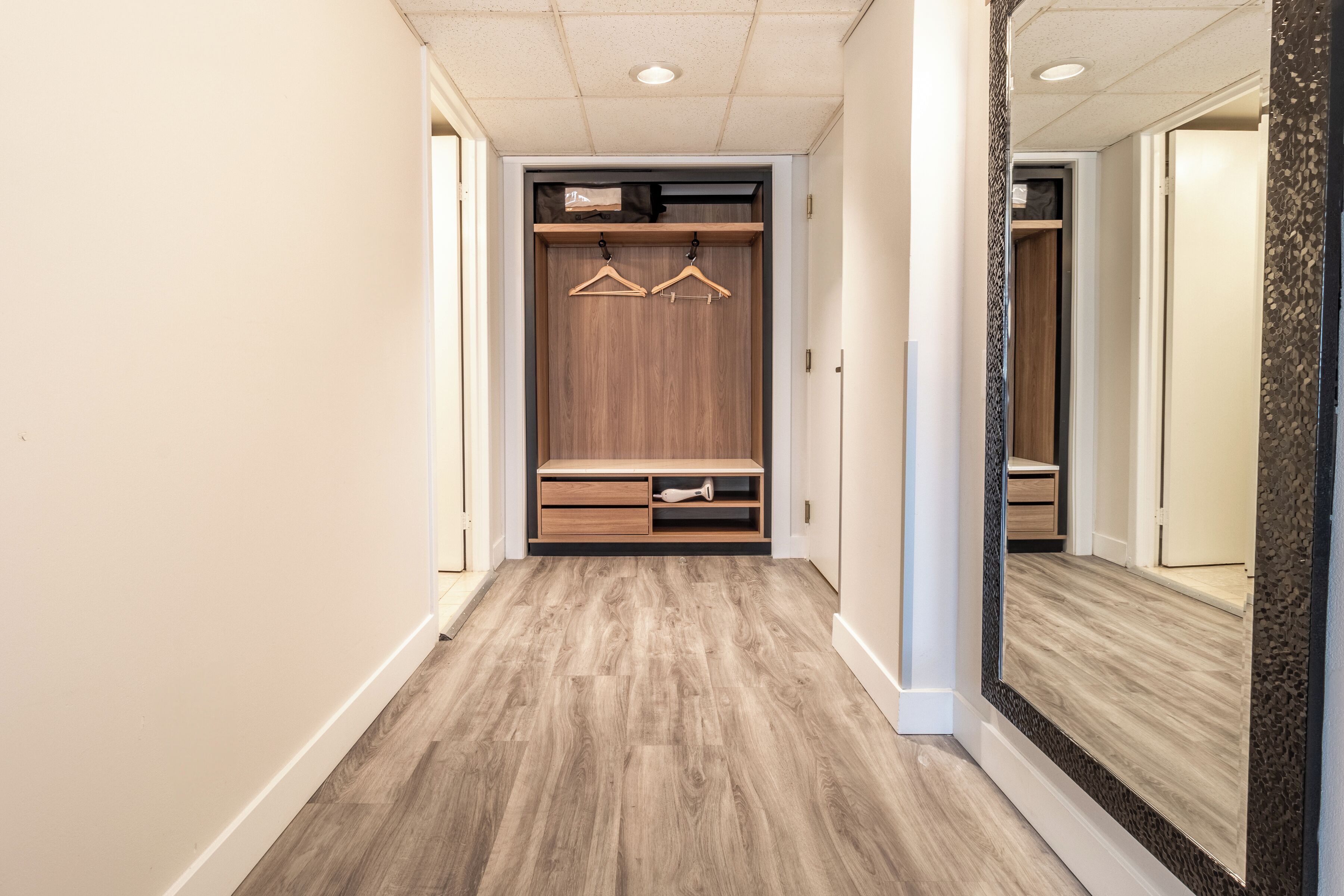 A hallway with a wooden floor, a mirrored wall, and a wooden closet with hanging space.