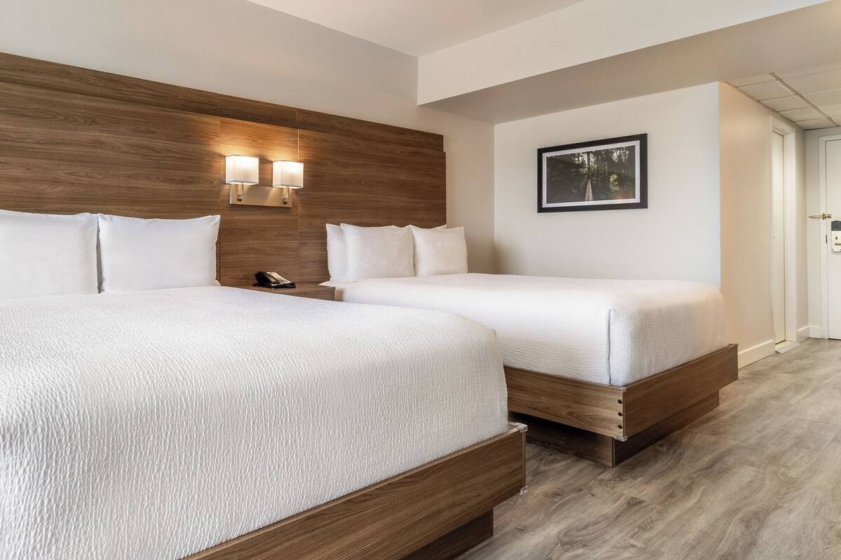 A hotel room with two beds, wooden headboard, bedside lamps, and a framed picture on the wall.