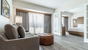Una habitación de hotel moderna con sofá, reposapiés y cama con cabecero de madera.