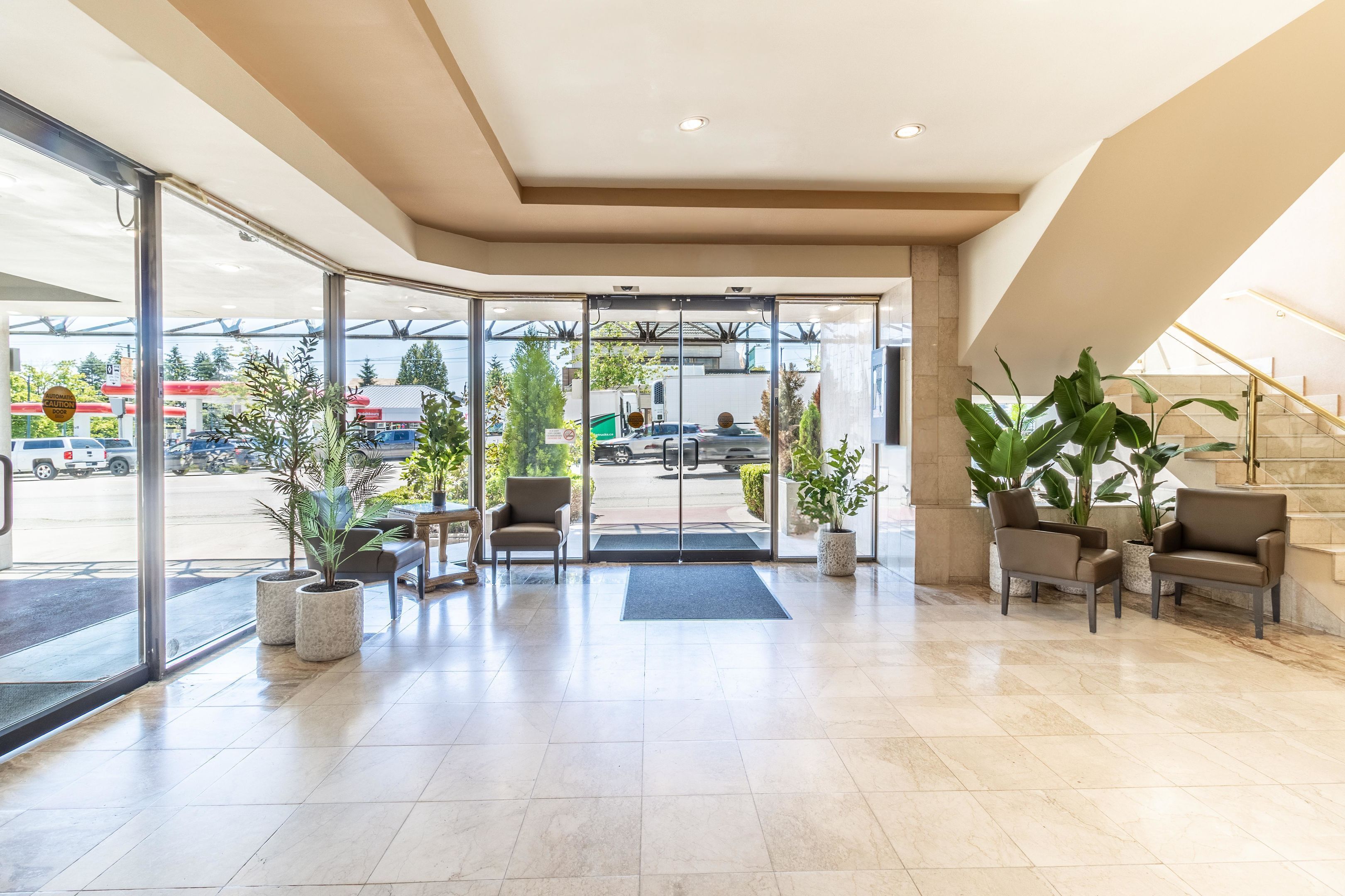 A hotel lobby with a glass entrance, seating area, and potted plants.