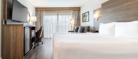 A hotel room with a large bed, a desk with a chair, a television, and a window with curtains.