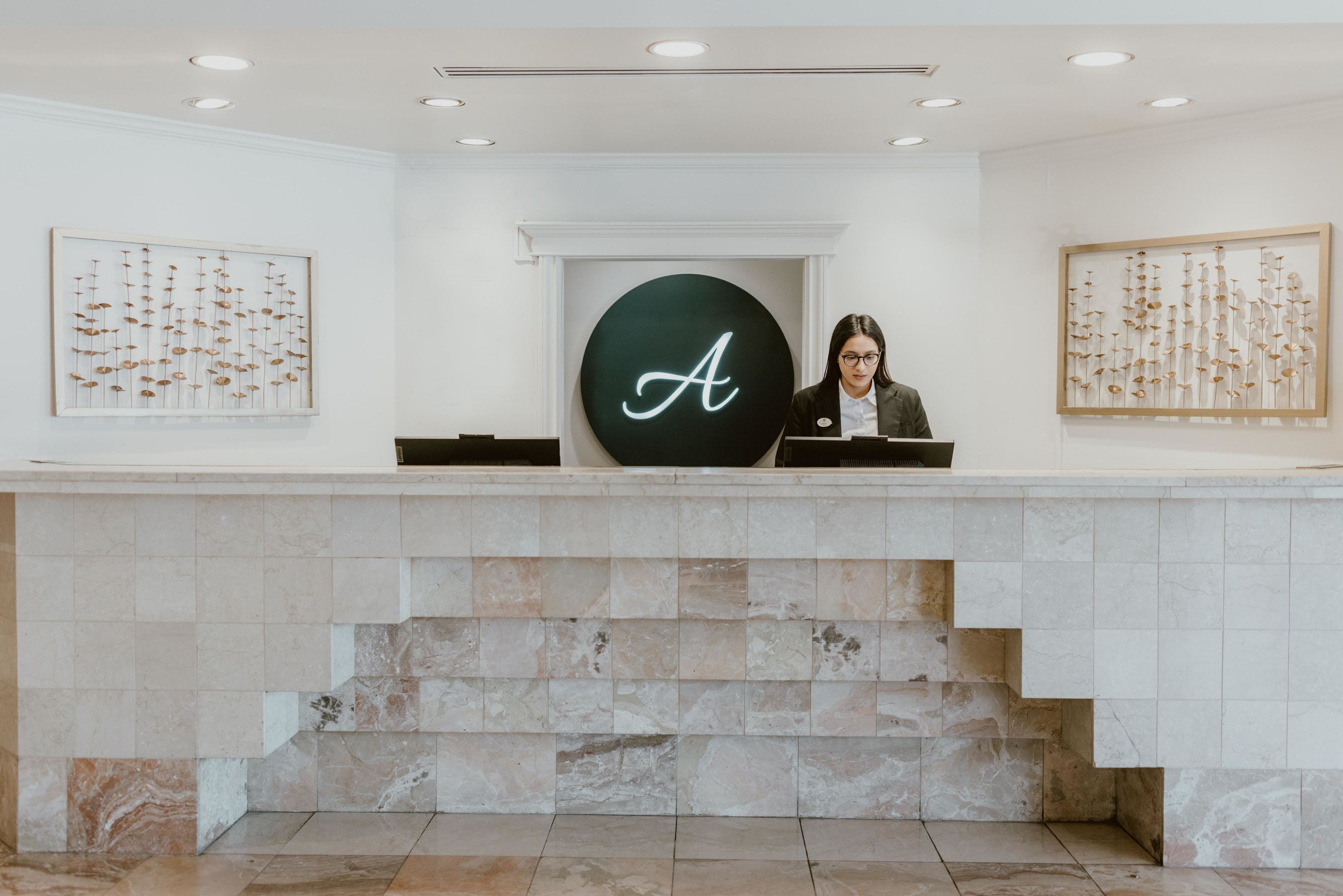 A reception desk with a large illuminated 'A' sign, marble steps, and framed botanical artwork on the walls.