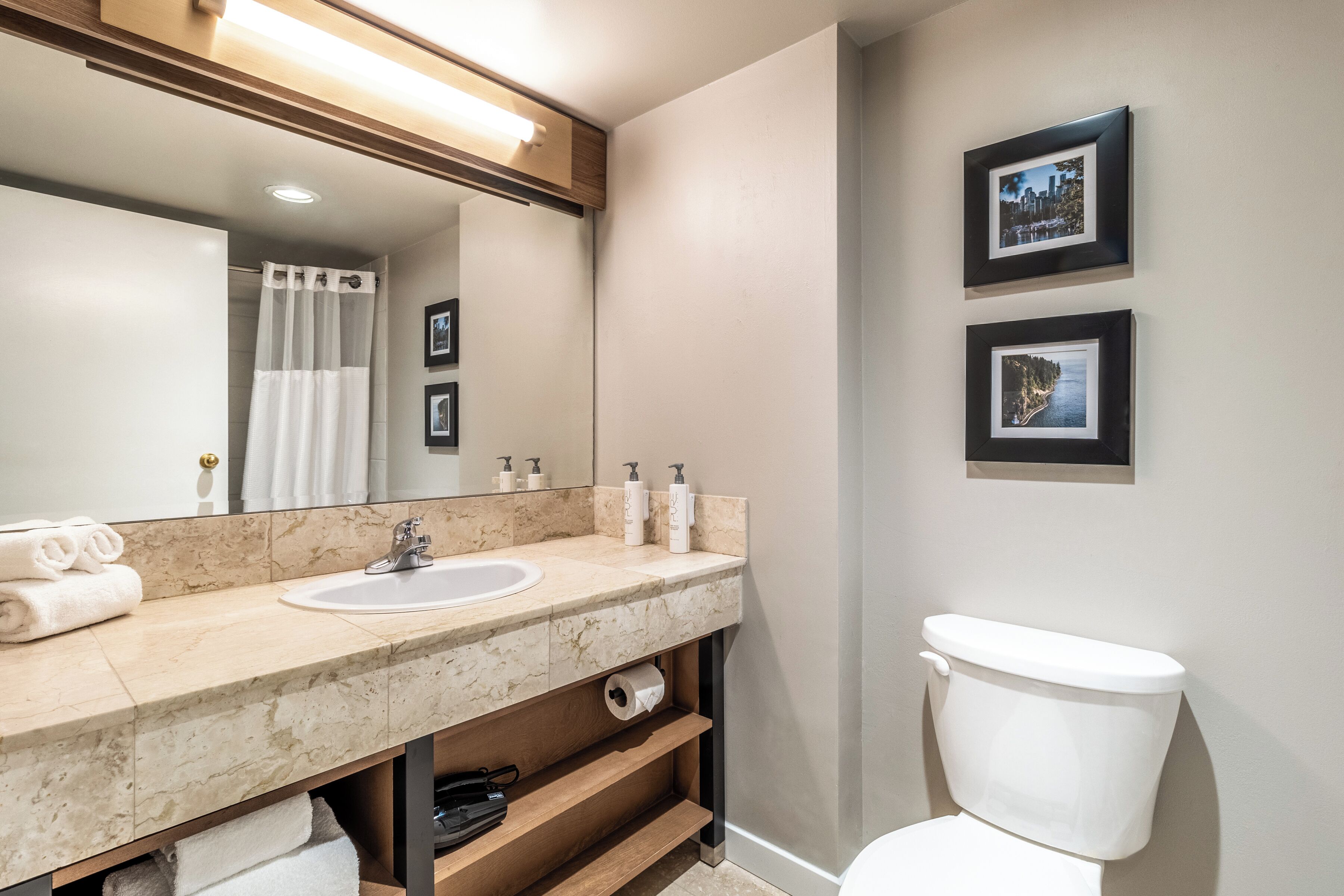 A bathroom with a marble sink, a toilet, and two framed pictures on the wall.