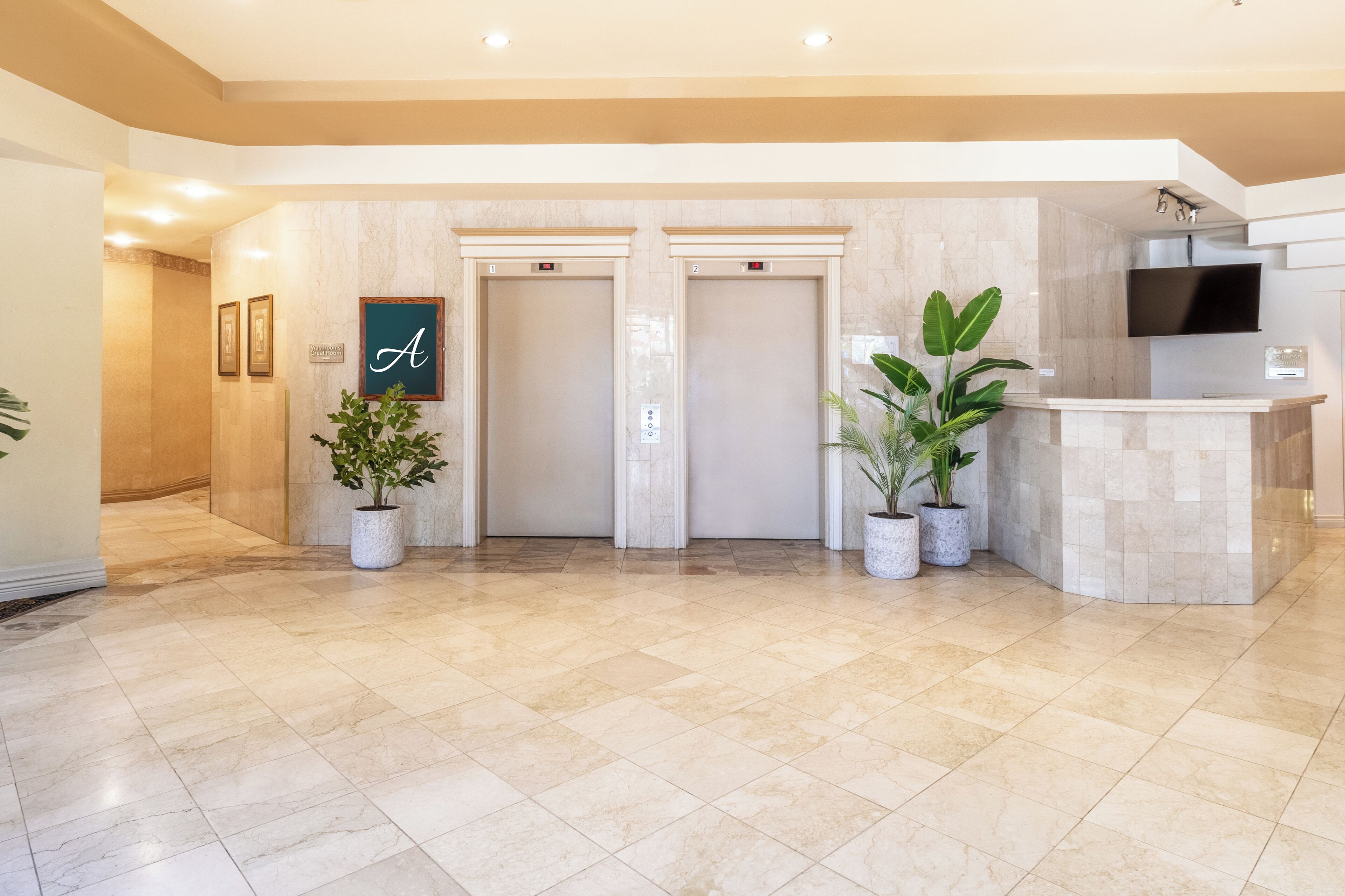 A hotel lobby with two elevators, a reception desk, and potted plants.