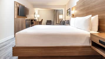 A modern hotel room with a large bed, a flat-screen TV, a desk with a lamp, and a seating area with chairs.
