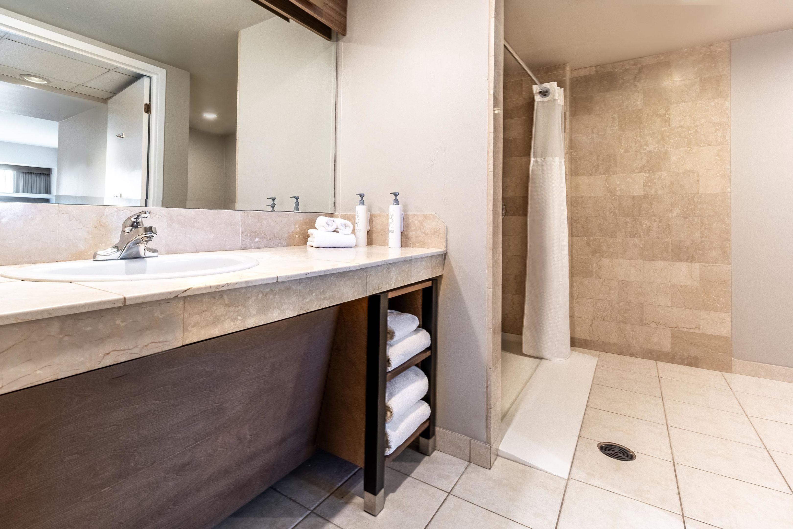 A modern bathroom with a large sink, mirror, and shower area.