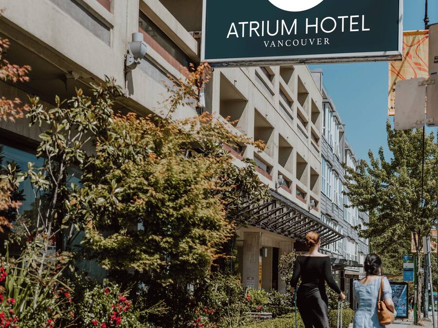 Un cartel del Hotel Atrium en Vancouver, mostrando un edificio moderno con balcones y un cielo despejado.
