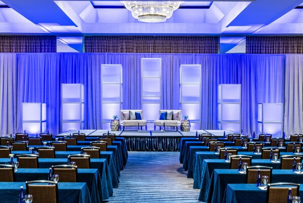 Un salón de conferencias con un escenario, filas de mesas y sillas.