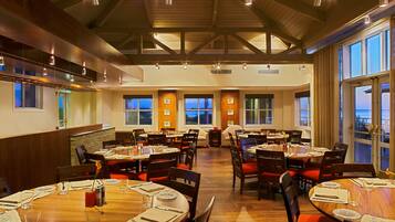 A restaurant with multiple dining tables, wooden floors, and large windows offering views of the outside.