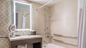 Un baño moderno con tocador, bañera, ducha con cabezal de ducha de mano y jabonera de vidrio.