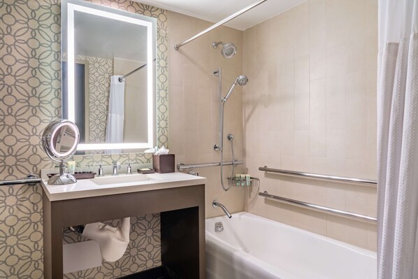 Un baño moderno con tocador, bañera, ducha con cabezal de ducha de mano y jabonera de vidrio.