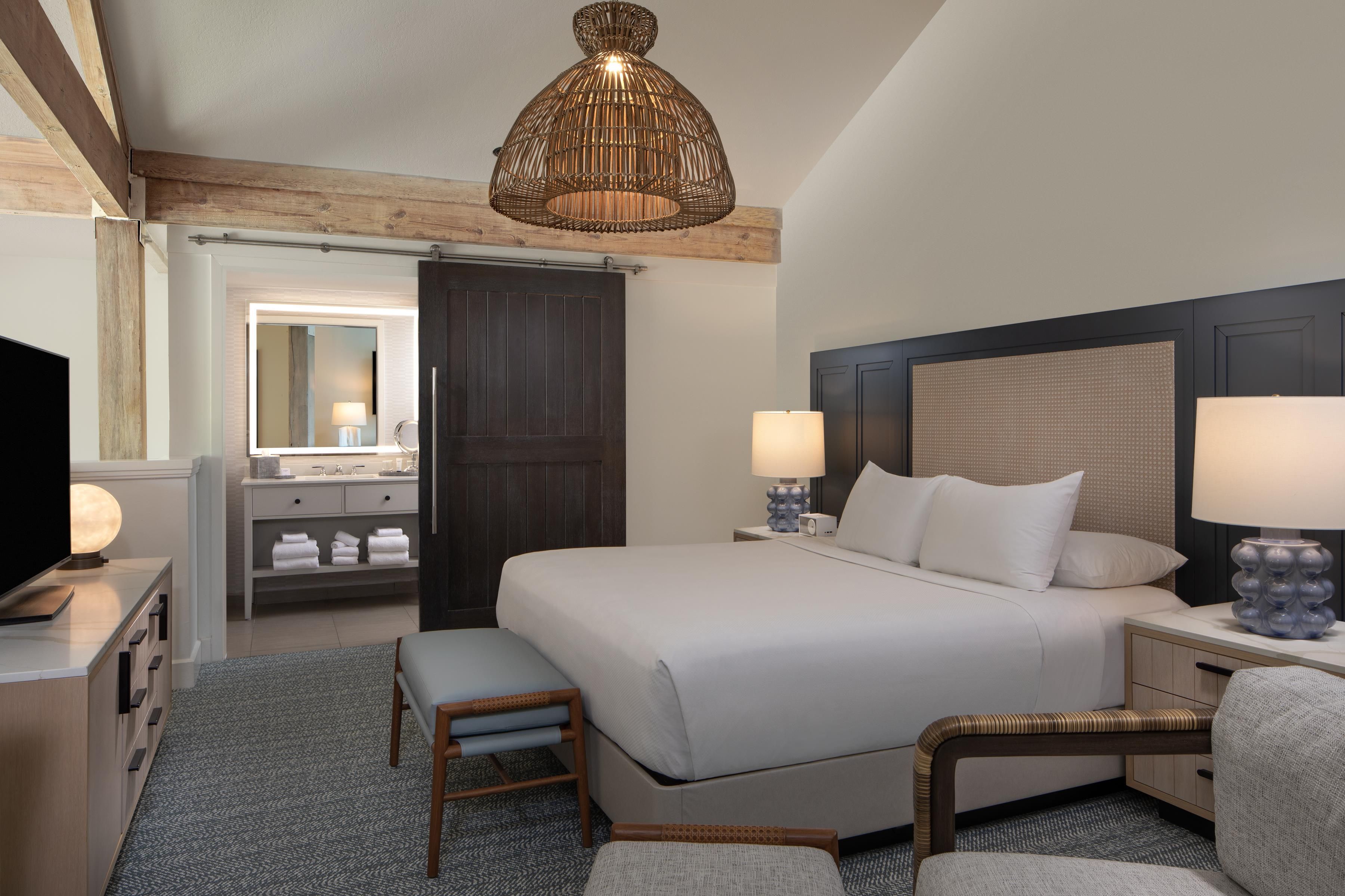 A hotel room with a bed, bedside lamps, a television, a mirror, and a wardrobe.
